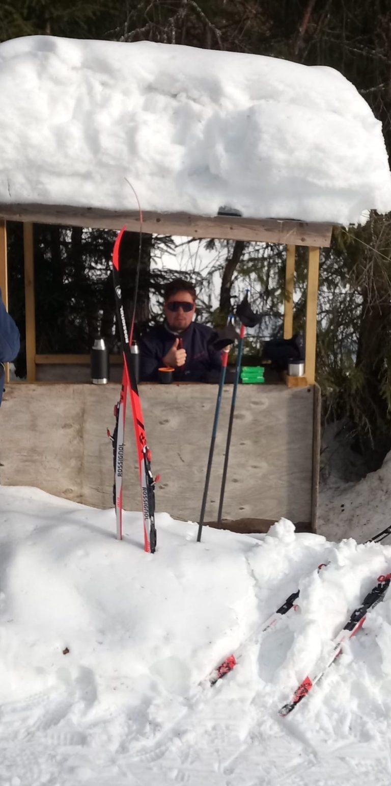 Mann in einem Kiosk im Schnee mit Skiausrüstung und verschneitem Dach.